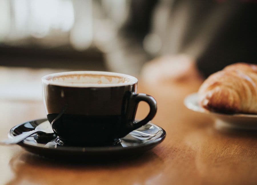 A closeup of a latte on a wooden table with a croissant.