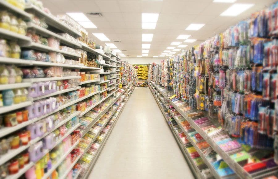 A look down the aisle of a dollar store with the florescent lights shining above.