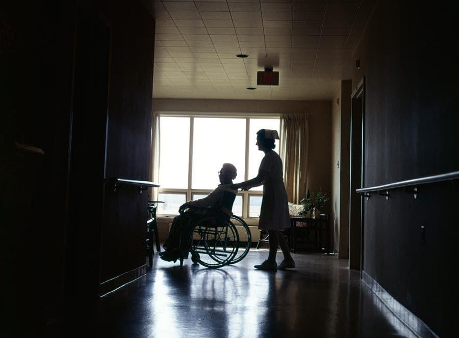 A nurse pushing a woman in a wheelchair in a nursing home.