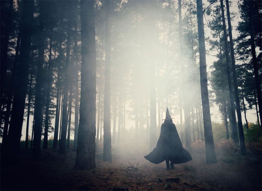 A witch walking through a foggy forrest.